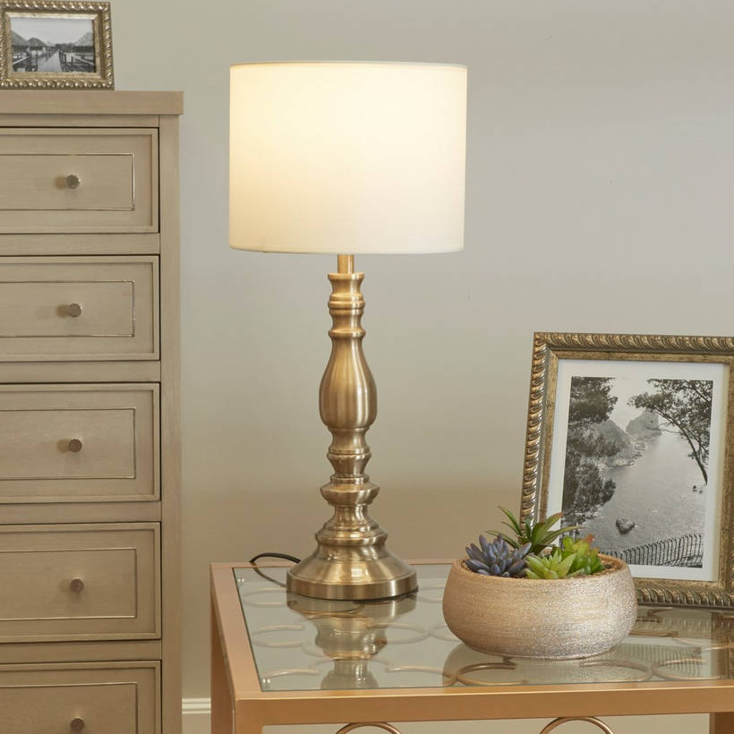 Decorative table lamp on a side table with a plant and framed picture in a room.