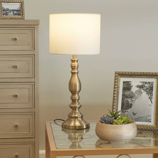 Decorative table lamp on a side table with a plant and framed picture in a room.